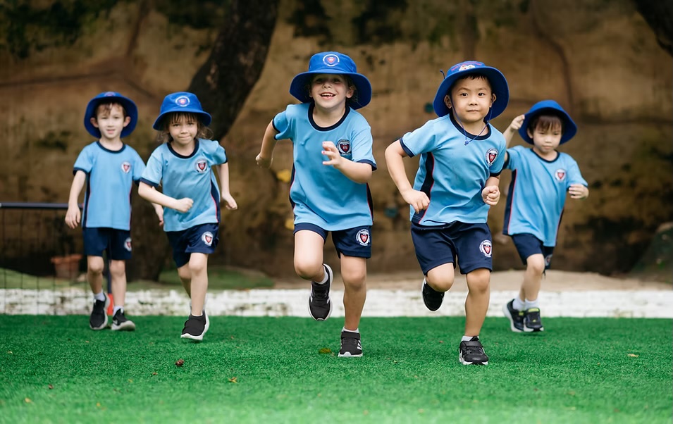 Young AISB students running across the school sports field in PE uniform