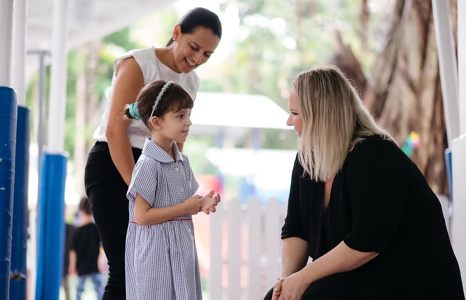 Two AISB teachers talking with a young student beside the playground