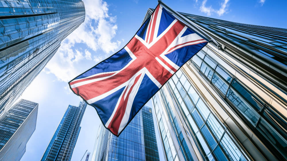 A Union Jack flag flying between glass office towers in a financial district